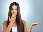 Portrait of a young mixed race beautiful woman standing looking shocked and surprised while showing a space with her hand against a grey background. Hispanic female having a ecstatic expression on her face