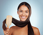 Portrait of a beautiful young mixed race woman brushing her healthy strong hair against a grey studio background. Hispanic female grooming her hair
