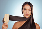 Portrait of a beautiful young mixed race woman brushing her healthy strong hair against a grey studio background. Hispanic female grooming her hair