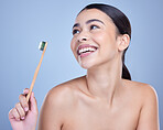 A smiling mixed race young woman with glowing skin posing against blue copyspace background while brushing her teeth for fresh breath. Hispanic model using toothpaste to prevent a cavity