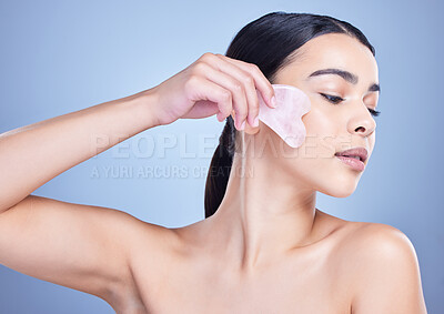Buy stock photo A beautiful mixed race woman using a rose quartz gua sha to reduce wrinkles and promote cell renewal. Young hispanic woman using anti ageing tool against blue copyspace background