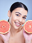 Portrait of a happy mixed race woman holding a grapefruit. Hispanic model promoting the skin benefits of citrus against a blue copyspace background