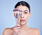 Studio Portrait of a beautiful mixed race woman posing with a collection of makeup brushes during pamper routine. Hispanic model with cosmetic tools standing against a blue copyspace background