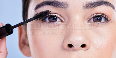 Buy stock photo Closeup portrait of a beautiful young mixed race woman with glowing skin posing against blue copyspace background. Hispanic woman with natural looking eyelash extensions applying mascara