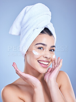 Buy stock photo Studio Portrait of a beautiful smiling mixed race woman applying cream to her face. Hispanic model with glowing skin and wet hair against a blue copyspace background