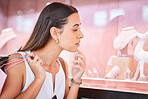 Young woman looking at jewellery on display through a window during a shopping spree in a mall. One female only enjoying retail therapy. Shopaholic holding bags and deciding whether to buy accessories