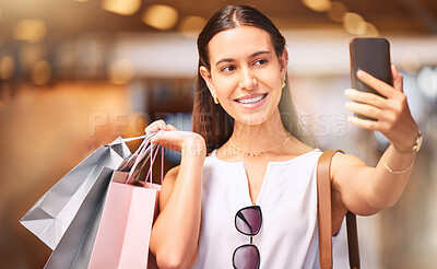 Buy stock photo Trendy young woman taking selfies on a cellphone during a shopping spree in a mall. One female only enjoying retail therapy while taking pictures. Happy shopaholic holding bags and making a video call