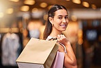 Portrait of a Young mixed race woman during a shopping spree in a mall. One hispanic female only enjoying retail therapy. Shopaholic holding bags smiling and looking happy while walking in a shopping mall