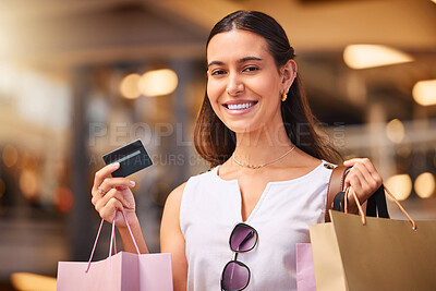 Buy stock photo A young mixed race woman holding a bank card while carrying bags during a shopping spree. Young brunette woman smiling while purchasing items with her credit card in a shopping mall. A little retail therapy is never a bad idea