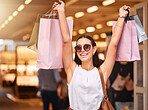Portrait of a Young mixed race woman wearing sunglasses during a shopping spree in a mall. Hispanic female enjoying retail therapy while looking excited. Shopaholic holding bags smiling and looking happy while standing in a shopping mall