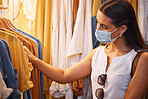 Female wearing a mask while shopping. Woman choosing an outfit at a store. Corona virus won't stop her from a shopping spree. Spending money on trendy fashion while protecting herself from a pandemic