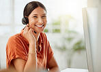 Portrait of one happy young hispanic female call centre telemarketing agent talking on a headset while working on a computer in an office. Confident and friendly mixed race business woman consultant operating helpdesk for customer service support