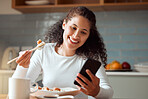 Woman eating sushi and using her cellphone. Young woman sending a text on her smartphone while eating seafood. Happy woman enjoying a meal at home. Young girl eating savoury fish