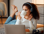 Woman using the internet on her laptop. Young woman drinking tea and listening to music. Young girl enjoying a cup of coffee using her laptop. Woman lying on her floor drinking a cup of tea.