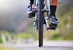 Closeup of one woman cycling outside. Sporty fit female athlete with her feet on bicycle pedals while riding a bike on a road for exercise. Endurance and cardio during a workout and training