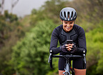 One athletic young woman using a cellphone while cycling outside on a bicycle. Sporty fit female wearing a helmet and taking a break to text, browse online social media and use a navigation app