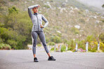 Active and fit young woman taking a break from exercising outdoors. Athletic female wiping sweat from her forehead after a jog or run outside. Woman looking tired but determined to continue her workout