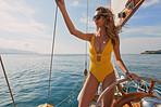 Young woman in yellow swimwear holding yacht rigging looking at the ocean steering boat. Smiling young woman in yellow swimsuit steering boat looking at the ocean holding onto rigging cables