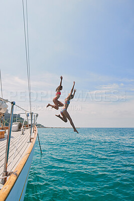 Buy stock photo Two excited friends jumping off a boat into the ocean to swim during cruise. Two cheerful women in bikinis jumping off a boat to swim in the ocean together on holiday cruise
