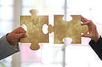 Two businesspeople holding and fitting puzzle pieces together in an office at work. Business professionals solving a jigsaw problem