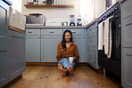 Young cheerful mixed race woman drinking a cup of coffee while using her phone alone in the morning in the kitchen. One happy cheerful hispanic female enjoying a cup of tea while using social media on her phone at home