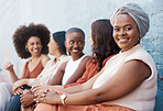 Young african american businesswoman sitting in a line with her coworkers against a wall outside in the city. Black female smiling while sitting outdoors with her colleagues
