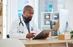 Mature african american doctor checking a patients chart. Focused gp reading a chart on a clipboard. Serious doctor reading a patients report. Professional physician reading a medical document