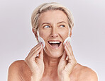 One beautiful mature caucasian woman isolated against a grey studio background and using cotton pads on her face. Senior practising skincare routine and cleansing her face with two hands for soft skin