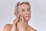 Portrait of one mature caucasian woman popping a zit during a skin care routine while posing against a grey copyspace background. Older model with a pimple targeting acne in a studio