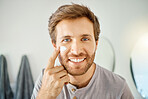One handsome man applying cream or moisturiser to his face in a bathroom at home. Caucasian male using a lotion or sunscreen in his apartment