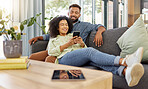 Happy young mixed race couple smiling while using a phone together at home. Cheerful hispanic boyfriend and girlfriend bonding and using social media on a smartphone in the lounge at home