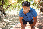 Exhausted young man standing with hands on his knees while taking a break from exercising in a park trying to stay fit. Athletic hispanic male resting and catching his breath after a run