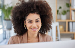 Closeup portrait of one young smiling African American woman using a desktop while sitting at a desk in her office job. Black woman with an afro at her job. Mixed race woman smiling looking positive