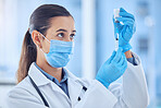 Young mixed race female doctor wearing a mask while preparing a vaccine at a hospital. Serious hispanic female doctor standing and extracting liquid from a vial with a syringe at a clinic