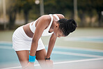 Tired tennis player taking a break during a match. Young athlete resting during tennis practice. African american tennis player relaxing after a tennis match. Woman tennis match exercise