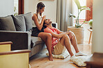 Loving young caucasian couple sitting together at home spending time and happy to be together. Happy young woman sitting on couch while her boyfriend sits between her legs as she plays with his hair and gently massages his head