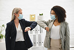 Two diverse colleagues talking and greeting each other with their elbows while wearing masks to protect from infection of a virus. Businesswomen joining their elbows to greet in an office at work