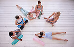 Group of women relaxing in yoga class from above. Friends talking, being social in pilates class. Women bonding in yoga class. Young women sitting on the floor in yoga class from above