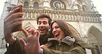 Cheerful young couple taking selfies on a cellphone in front of Notre Dame