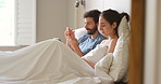 A content young couple spending time in bed together while using their smartphones and digital tablet