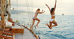 Happy friends excitedly jumping into the ocean from a boat sailing around Italy. Two women on holiday jumping off a boat together into the ocean to swim. Women jumping into the ocean from a boat